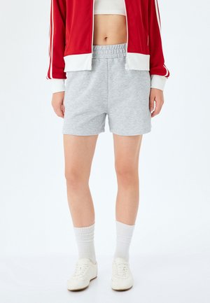 Grijze, lichtgewicht katoenen shorts met een elastische tailleband. Gecombineerd met een rode zip-up jack. Witte sneakers en geribbelde sokken maken de look compleet.