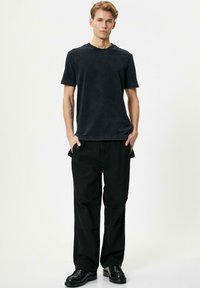 Camiseta de algodón negra con un corte relajado y escote redondo, combinada con pantalones anchos negros y zapatos de cuero negros.