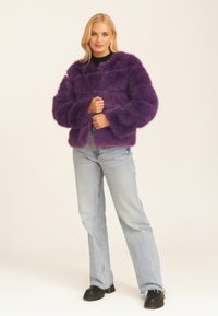 Purple faux fur jacket with a cropped design, wide sleeves, and a soft texture. Paired with light blue jeans and black chunky footwear.