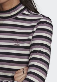 Prúžkovaný dlhý rukáv top v purpurovej, černej a bielej farbe z bavlneného zloženia. Má vysoký golier a vyšívané logo Adidas na hrudi.