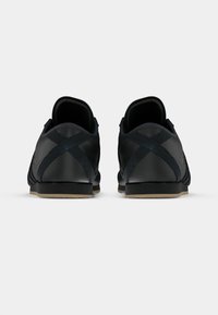 Črni športni čevlji z gladkim usnjenim zaključkom, nizkim rezom, okroglim petnim delom in prečnim šivom. Gumijast podplat.