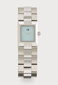 Reloj rectangular de acero inoxidable plateado con una esfera turquesa clara, dos agujas y un pequeño logo. Presenta una pulsera de metal con eslabones.