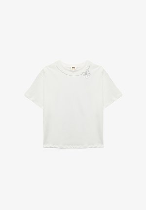 Hvid kortærmet t-shirt lavet af blødt stof, med en buet halsudskæring prydet med små prikkede dekorationer og et sløjfedesign.