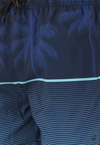 Shorts de bain bleus ornés d'un motif de palmiers et de rayures horizontales dans des nuances variées de bleu. Taille élastique avec cordon de serrage.
