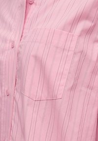 Ροζ πουκάμισο με κουμπιά, λεπτές κάθετες ρίγες και ραμμένη ορθογώνια τσέπη στο στήθος στην αριστερή πλευρά.