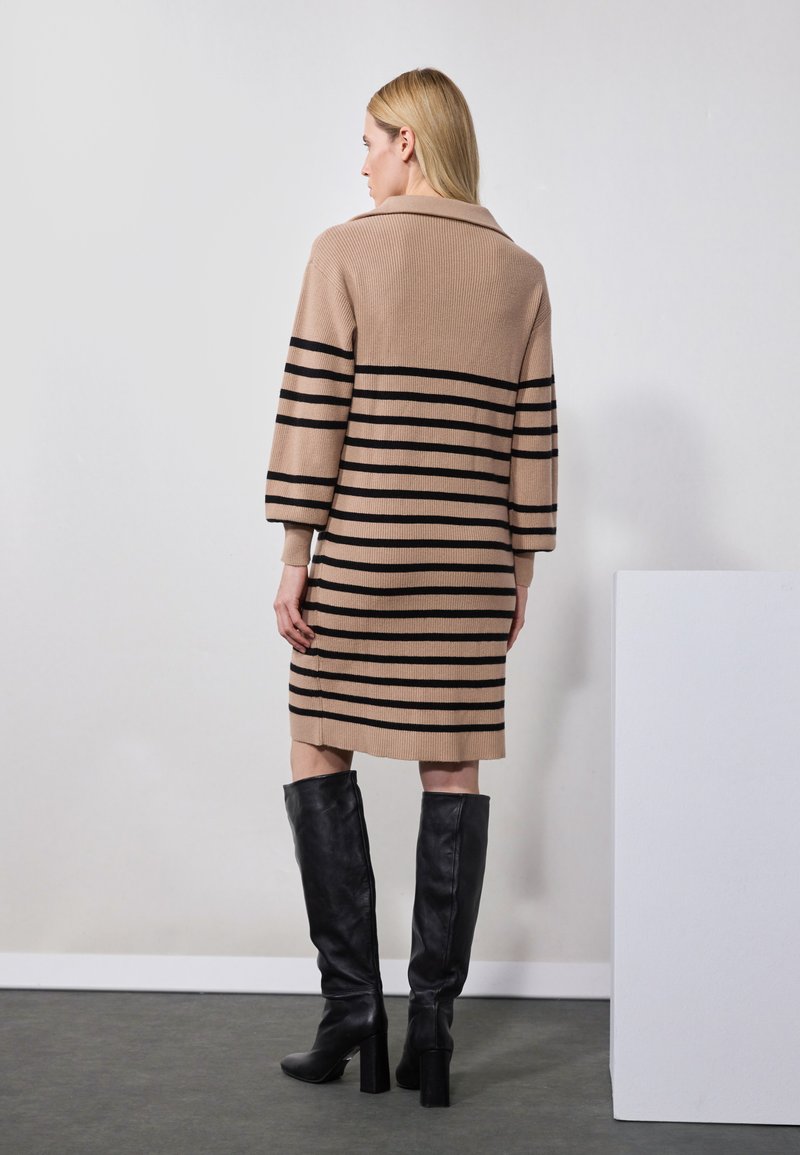 Vestido de punto a rayas beige con cuello y mangas hasta el codo. Presenta rayas horizontales negras y un corte holgado. Llevado con botas negras hasta la rodilla.