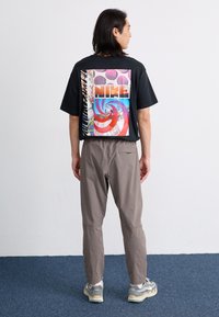 Tricou negru cu mâneci scurte, având o grafică mare multicoloră pe spate, asortat cu pantaloni elastici de culoare gri deschis și adidași gri.