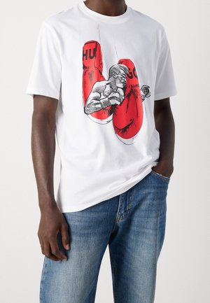 Mand iført hvid t-shirt med røde boksehandsker og en bokserillustration, kombineret med blå jeans.