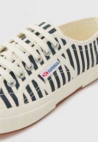 Canvas sneakers with blue and white horizontal stripes, cream laces, rubber sole, and a red and blue "Superga" logo tag.