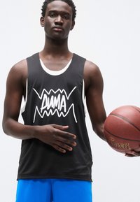 Μαύρη αμάνικη φανέλα μπάσκετ με λευκό λογότυπο, με αντίθετη λευκή επένδυση. Μπλε αθλητικό σορτς. Παίκτης που κρατάει μπάλαν μπάσκετ.