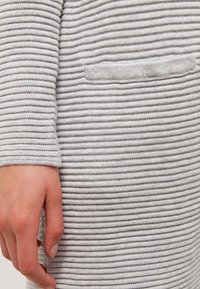 Tessuto grigio a coste con strisce orizzontali, caratterizzato da un piccolo dettaglio della tasca. Ingrandimento di una mano che tiene il materiale textures.