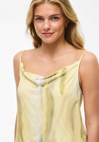 Top fluido sin mangas en tela suave; cuenta con cuello drapeado; amarillo pastel con patrones abstractos en verde y gris; textura ligera y suave.