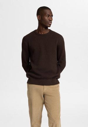 Brauner, strukturierter Pullover mit Rundhalsausschnitt, kombiniert mit hellbraunen Cordhosen. Der Pullover hat gerippte Bündchen und einen gerippten Saum.