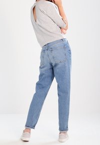 Top gris de manga corta con corte en la espalda, combinado con jeans de tiro alto en azul claro. Modelo usando zapatillas claras, de espaldas a la cámara.