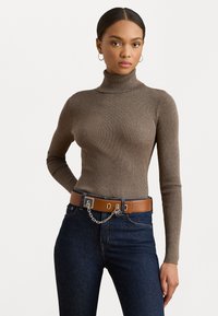 Bruine geribbelde coltrui gecombineerd met donkere spijkerbroek en een bruine riem met een kettingaccent. Gladde textuur en aansluitend design.