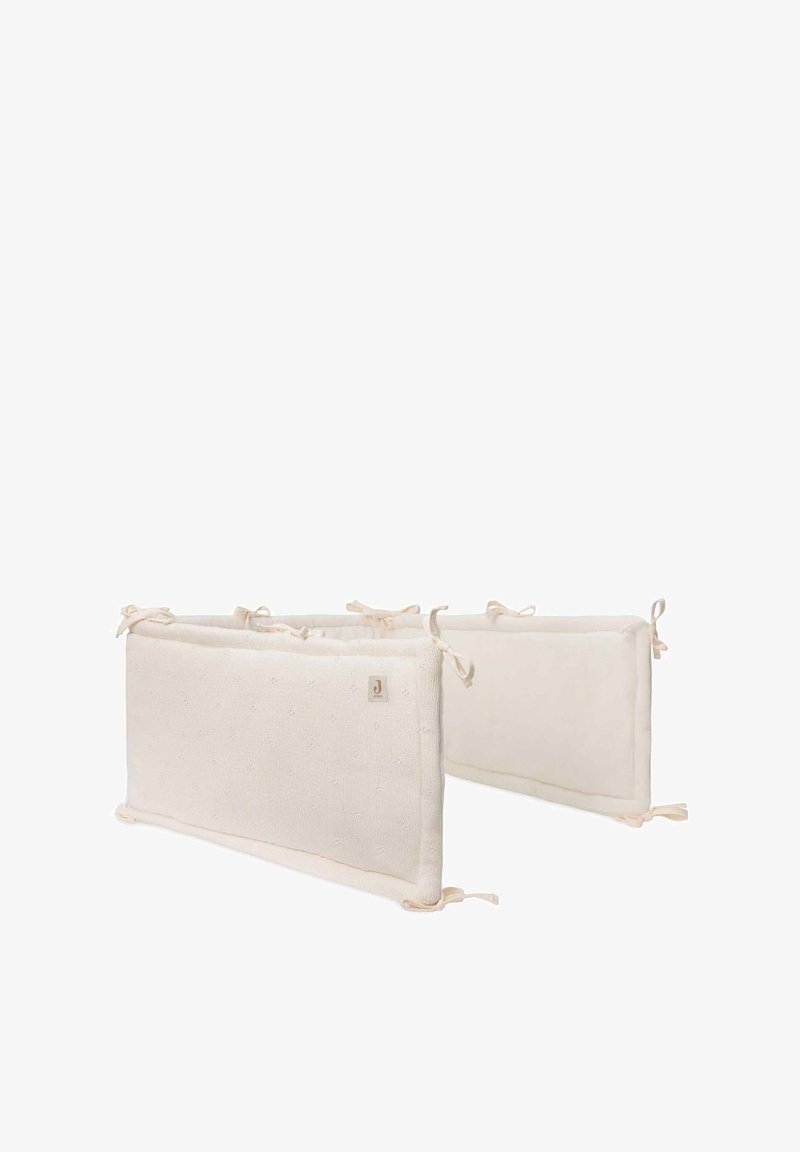 Coussins de protection en coton pour lit de bébé de couleur crème neutre, présentant un tissu texturé avec de petits points et des extrémités à nouer pour un maintien sécurisé.