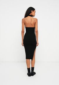 Μαύρο ριμπ μίντι φόρεμα με α strapless σχέδιο, διαθέτοντας ένα πλάι άνοιγμα και υλικό με υφή. Το μοντέλο φοράει μαύρα παπούτσια και κάλτσες.