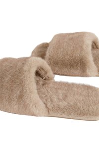 Zapatillas de felpa beige con una superficie suave y texturizada, que presentan un diseño sencillo sin hardware visible. Estilo de punta abierta redondeada.