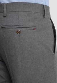 Pantaloni grigi, con texture, dotati di una tasca posteriore con un bottone marrone e una striscia colorata di accento. Vestibilità su misura, finitura del tessuto liscia.
