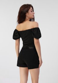 Sort off-shoulder top med puffede ærmer; struktureret stof. Matchet med tætsiddende sorte shorts med baglommer og detalje ved livet.