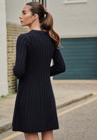 Marineblå strikket kjole med et tekstureret kabelmønster, lange ærmer og en udvidet kant, lavet af blødt, varmt stof.