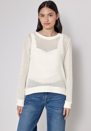 Maglione leggero in crema con un design a maglia aperta e testurizzata. Maniche lunghe, scollatura rotonda e polsini a coste. Abbinato a jeans blu.