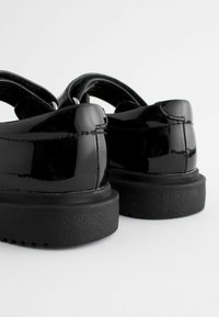 Chaussures en cuir verni noir avec une finition lisse, un talon bas et des bandes élastiques dotées d'une semelle en caoutchouc texturé.