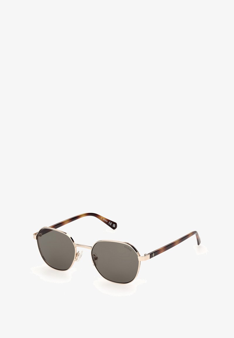 Gafas de sol con una montura de metal dorado y lentes de un gris oscuro. Las varillas tienen un patrón de carey, ofreciendo un diseño único y elegante.