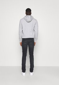 Szara bawełniana bluza z kapturem i długimi rękawami, w połączeniu z czarnymi dżinsami slim fit i białymi trampkami. Widok z tyłu.