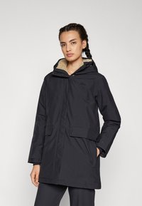 Parka noire imperméable avec capuche, dotée d'une douce doublure en fourrure brun clair, de poches avant et d'une fermeture éclair. Marquage minimaliste visible.