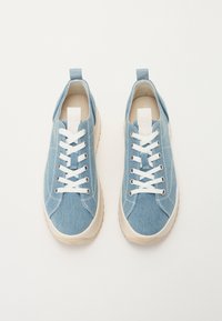 Sneakers in denim azzurro chiaro con lacci bianchi, una linguetta in tessuto sul tallone e una suola in gomma beige spessa; texture liscia e design piatto.