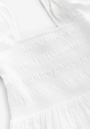 Abito bianco con corpetto arricciato, tessuto testurizzato e spalline larghe. Design fluido con un aspetto morbido e leggero.