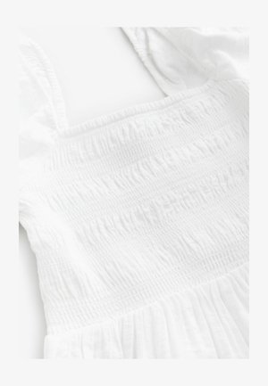 Valkoinen mekko, jossa on rypytetty yläosa, teksturoitu kangas ja leveät olkaimet. Suuri ja virtaava muotoilu, jossa on pehmeä, kevyt ilme.