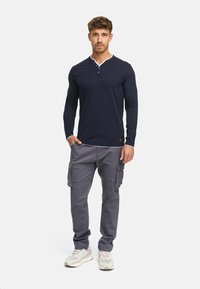 Navy long-sleeve henley shirt with white collar trim, paired with gray cargo pants featuring side pockets, worn with light sneakers.