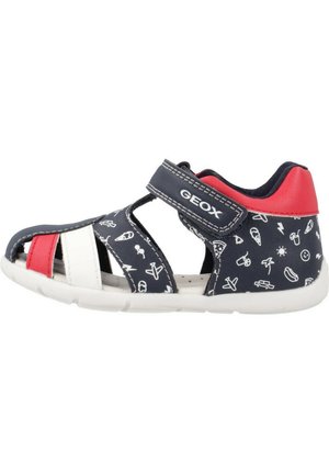 Sandalia azul y roja con diseño recortado, correa de velcro, acentos en blanco y rojo, que presenta patrones juguetones en el material azul.