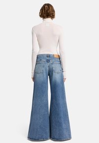 Laadulliset siniset farkut leveällä lahkeella ja vaalealla pesulla, joissa on suuret takataskut ja nahkapaikka vyötäröllä. Ribattu valkoinen pitkähihais top.