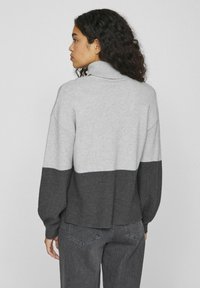 Suéter bloqueado en gris y gris oscuro con un alto cuello, corte holgado, textura acanalada y costuras de hombro caídas. Lleva puesta con jeans grises.