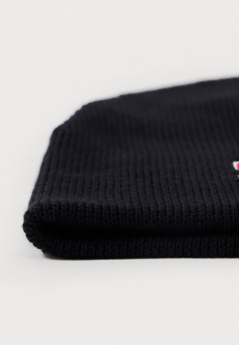 Bonnet en tricot noir avec une texture côtelée, présentant un rebord replié. Matière douce affichant un léger éclat sous la lumière. Aucune logo ni motif visible.