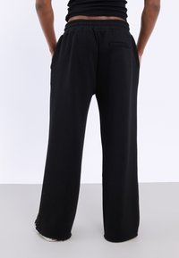 Zwarte, losse sweatpants met een trekkoord in de taille, zijzakken en een achterzak. Gemaakt van zachte materiaal met een gladde textuur.
