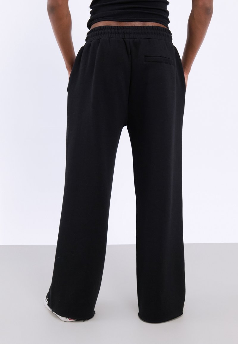 Zwarte, losse sweatpants met een trekkoord in de taille, zijzakken en een achterzak. Gemaakt van zachte materiaal met een gladde textuur.