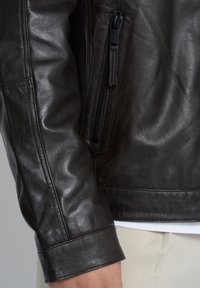 Brun læderjakke med en lynlåslomme på ærmet, glat tekstur, knaplukning ved manchetten og en tætsiddende design.