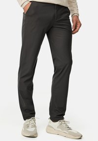 Pantalons anthracite, ajustés en tissu lisse. Dotés de poches latérales et de jambes effilées. Associés à des baskets texturées de couleur claire.