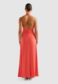 Coral halter maxi dress with a fitted bodice and ruched detailing at the back, flowing to the floor. Smooth fabric and open back design.