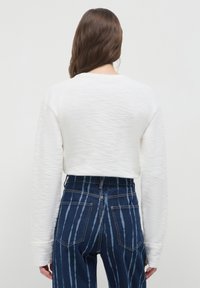 Maglione bianco corto con tessuto texturizzato e maniche lunghe, abbinato a jeans di denim blu con strisce verticali e tasche posteriori.