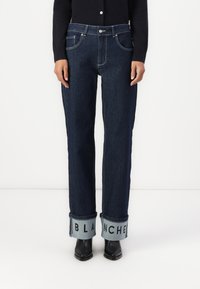 Jeans de mezclilla de pierna recta en azul oscuro con puños en azul claro que presentan el texto "BLANCHER". El tejido parece resistente y tiene una textura suave.