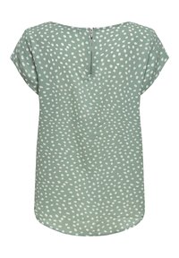 Blouse verte à manches courtes avec un motif de pois blancs irréguliers et une courte fermeture éclair au niveau de l'encolure arrière.