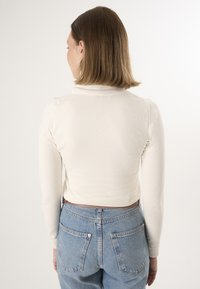 Haut blanc à manches longues avec un col haut, au design ajusté et en tissu texturé, associé à un jean taille haute bleu clair.