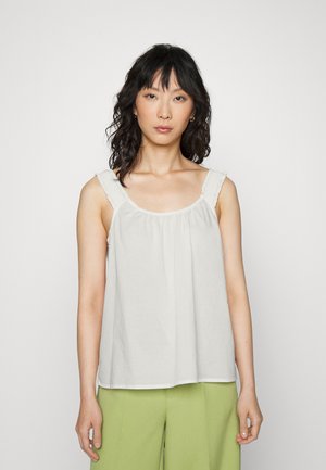 Blusa branca com alças franzidas, corte solto e decote arredondado. Usada com calças verdes de perna larga. Tecido suave e design simples.