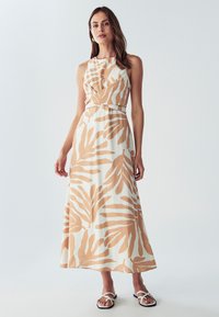 Maksi obleka v beli barvi z velikimi bež listnatimi vzorci. Ima brezrokavni dizajn, zategnjen pas in tekočo teksturo. V kombinaciji s ravnimi sandalami.