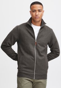 Donkergrijze zip-up jack met staande kraag, lange mouwen en voorzakken. Gemaakt van een gestructureerde stof met een soepele rits en leren details.